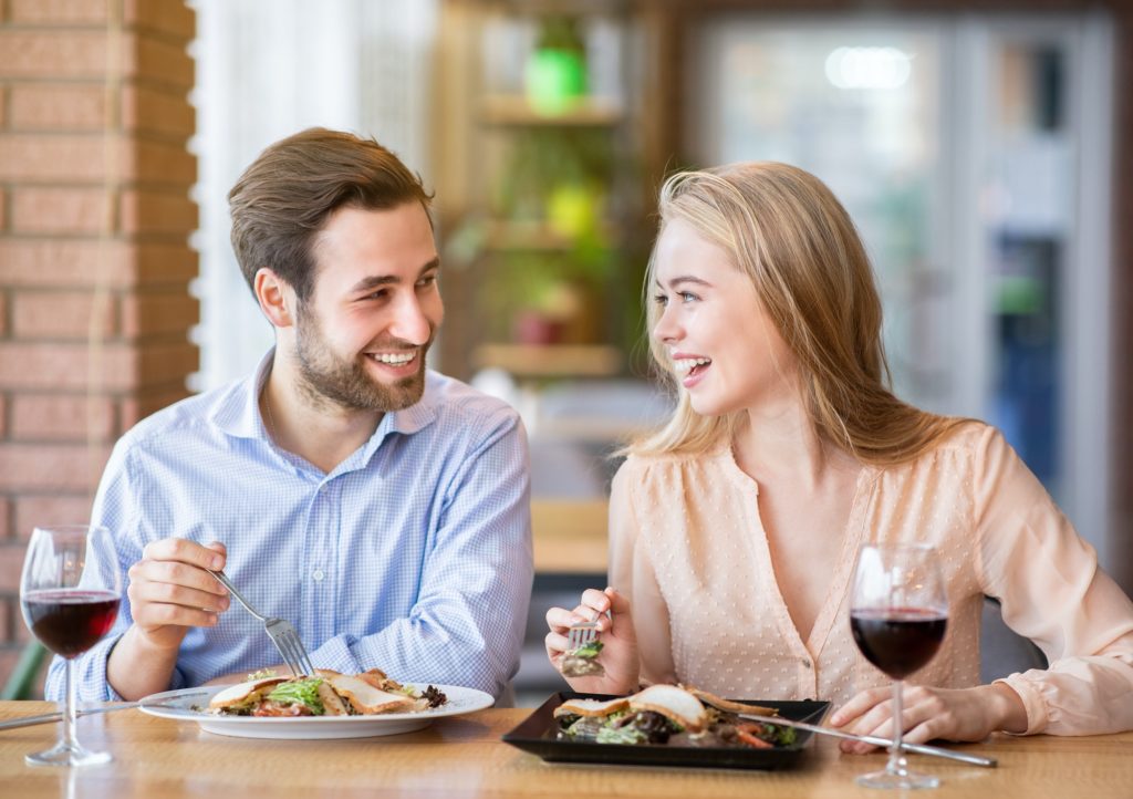 Lovely lady with her boyfriend eating salad and drinking wine, celebrating anniversary together at