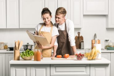 young couple cooking salad and looking at recipe book in kitchen