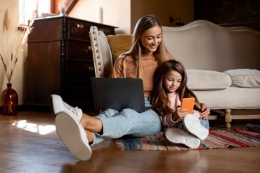 Happy woman and daughter using laptop and cell phone