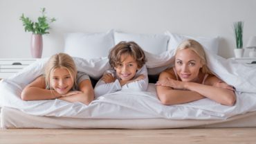 Babysitter and two childrens hiding in bedroom under covers in the morning