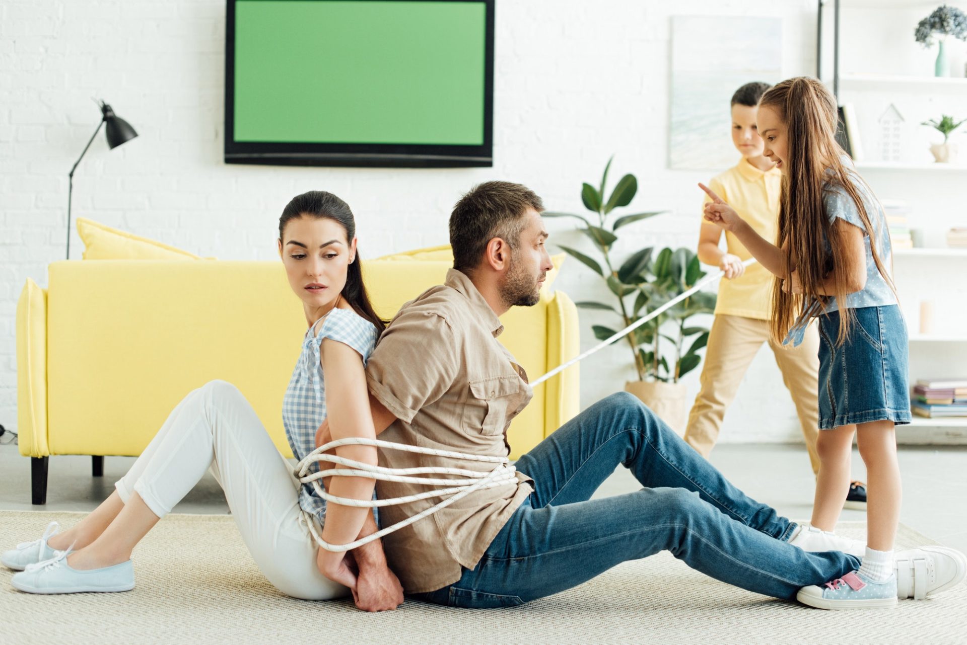 children tying parents with rope on floor at home, parenthood concept