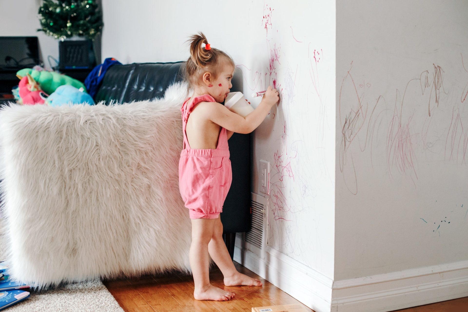 Cute toddler girl writing with marker on white wall in apartment home. adorable kid having fun.