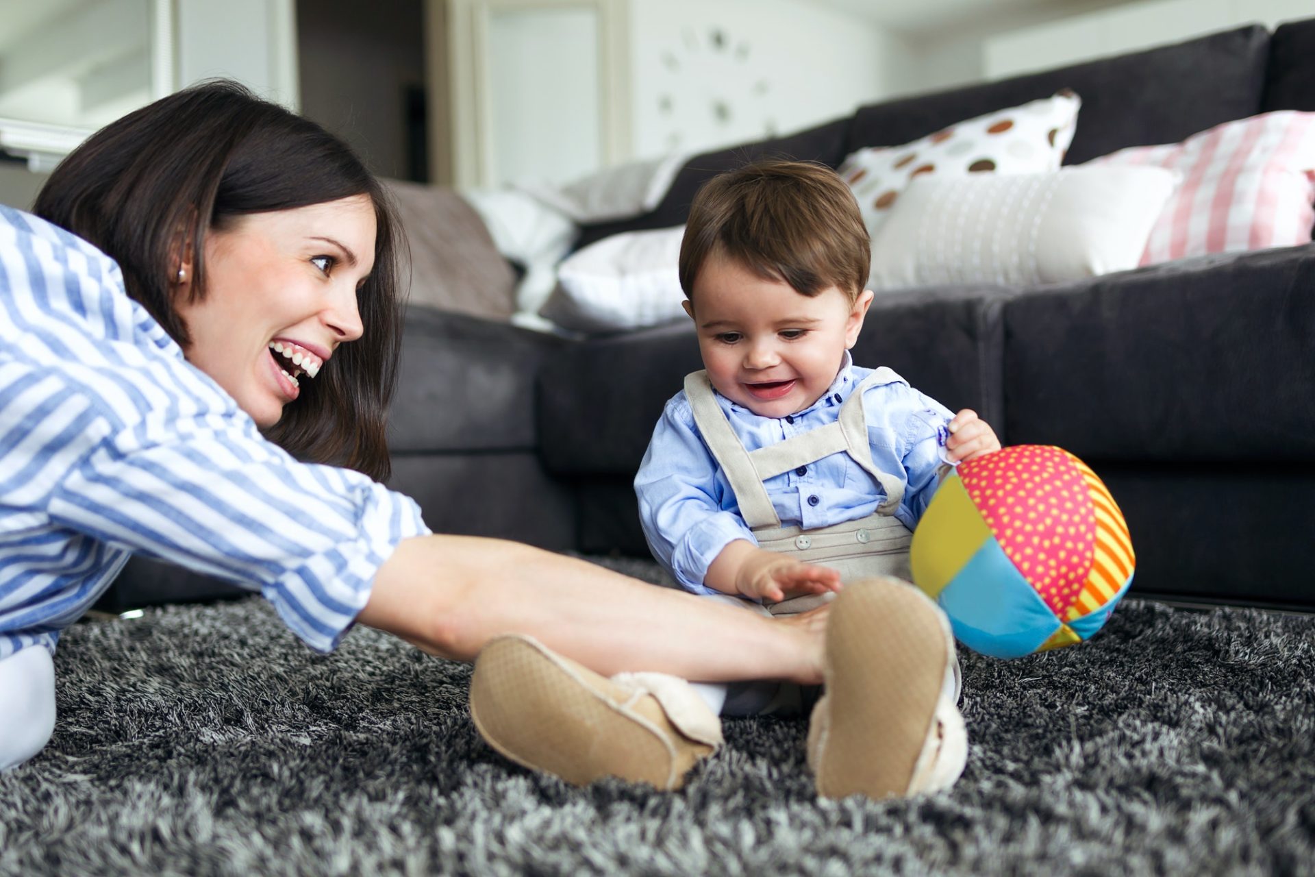Happy young mother with her baby playing on the floor of living room at home.