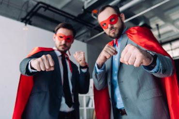 low angle view of handsome super businessmen in masks and capes showing fists in office