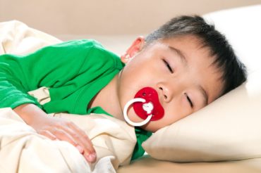 Portrait of a young boy sleeping with pacifier in mouth.