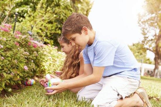 Two Children Having Easter Egg Hunt In Garden