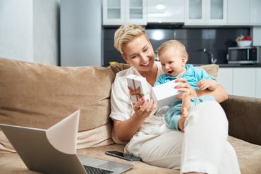 Woman with baby sitting on couch and opening present